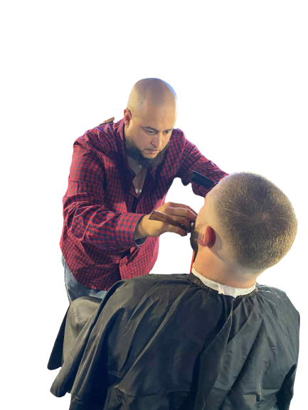 A barber in a red plaid shirt trims the beard of a seated client dressed in a black cape at his popular shop in Bartow.