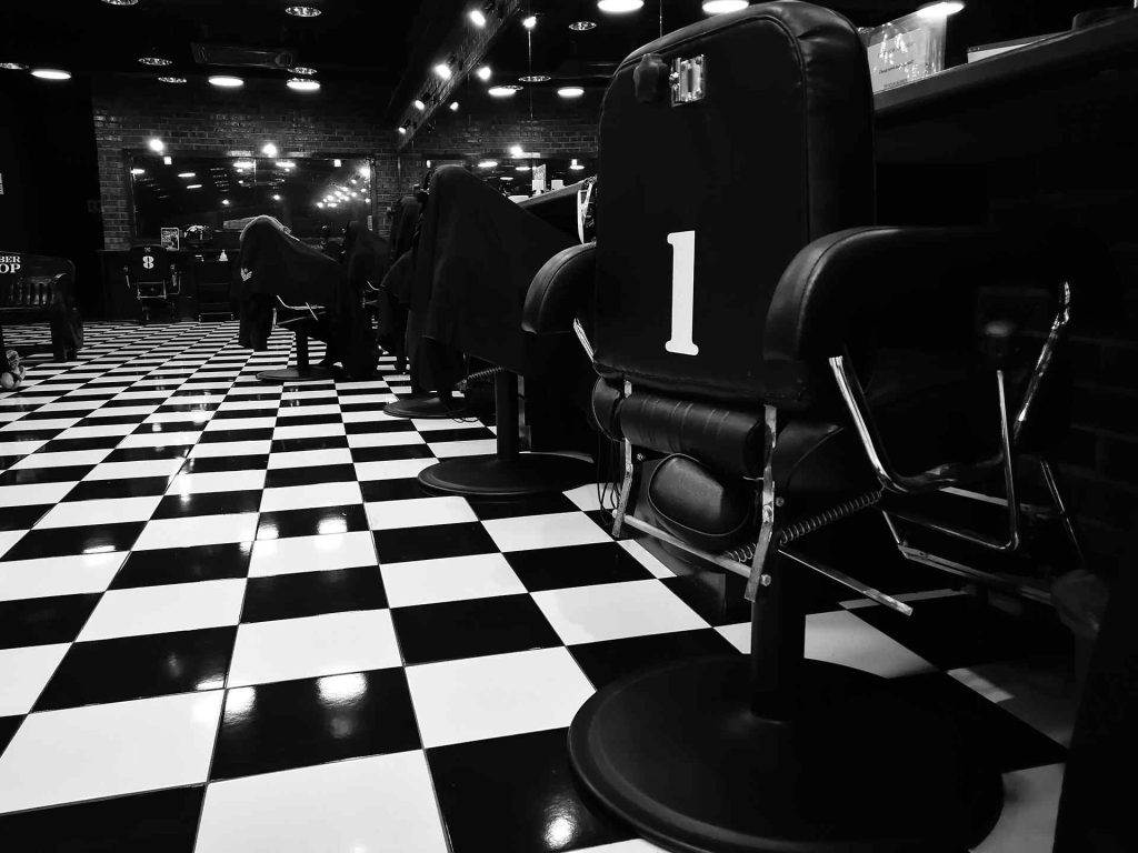 Black and white photo of a barbershop in Bartow, Florida, with checkered floor tiles and empty barber chairs. One chair is marked with the number 1.