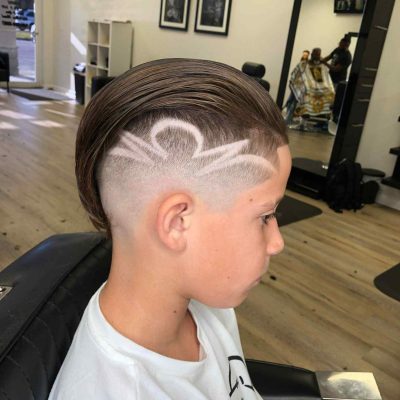 A young boy with a short undercut hairstyle featuring an artistic shaved design on the side, sitting in a barbershop chair, skillfully styled by a renowned barber in Bartow.