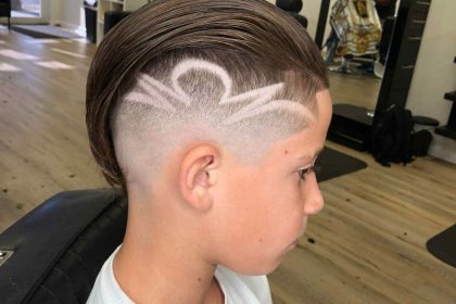 A young boy with a short undercut hairstyle featuring an artistic shaved design on the side, sitting in a barbershop chair, skillfully styled by a renowned barber in Bartow.
