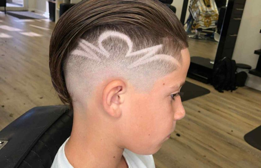 A young boy with a short undercut hairstyle featuring an artistic shaved design on the side, sitting in a barbershop chair, skillfully styled by a renowned barber in Bartow.