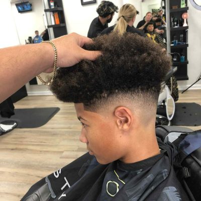 A person receives a haircut in a barbershop. Another individual is shaping their hair while they sit in a barber chair, with mirrors and barber tools visible in the background—a typical scene for a Barber in Bartow.