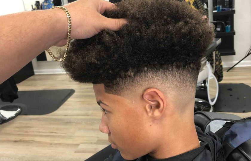 A person receives a haircut in a barbershop. Another individual is shaping their hair while they sit in a barber chair, with mirrors and barber tools visible in the background—a typical scene for a Barber in Bartow.