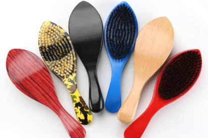 A collection of six Marathon Wave Brushes, each featuring a unique design and color—including red, yellow camouflage, black, blue, wood grain, and red-and-black mixed bristle patterns—arranged in a fan shape. Perfect for any barber in Bartow seeking a stylish set.